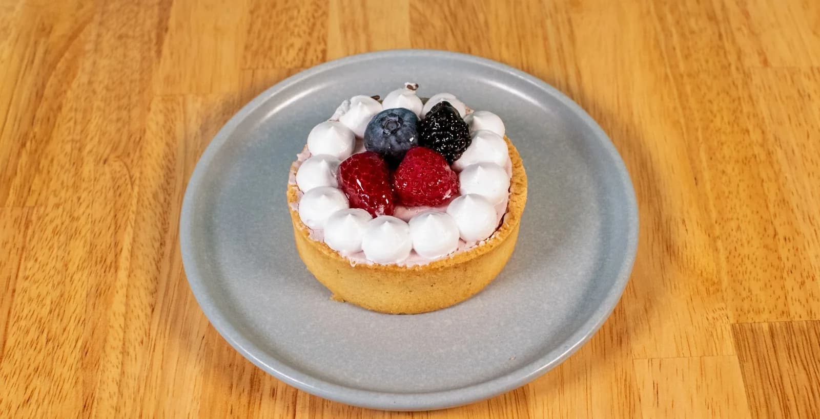 Mini tart with whipped cream, raspberries and blueberry on a gray plate