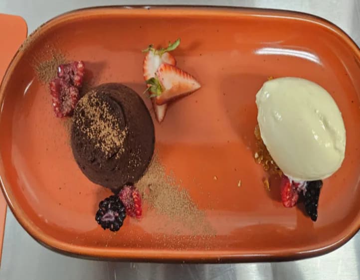 Petit gâteau with ice cream and berries on a terracotta plate